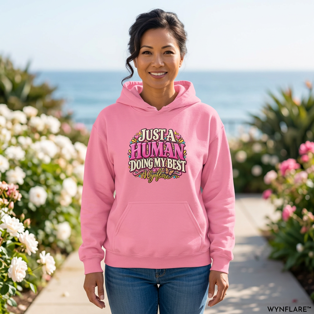 Woman wearing the azalea pink Just a Human Doing My Best hoodie in a sunlit coastal garden